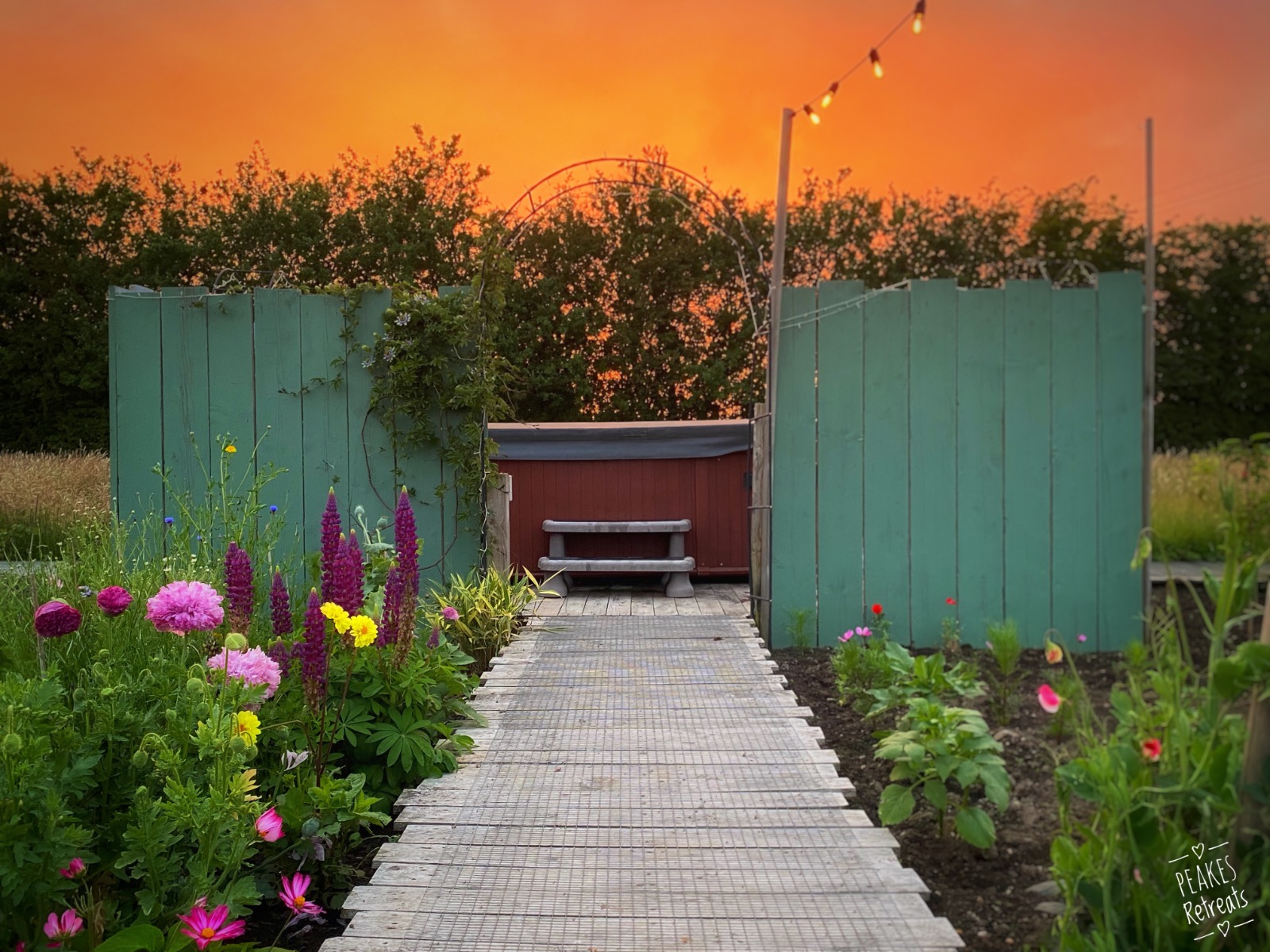 Outdoor Hot tub surrounded by beautiful flowers and a blazing sunset at Peake's Retreats